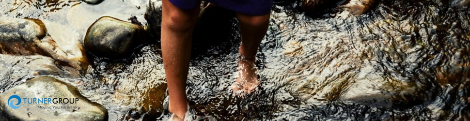 A person crossing a rocky river barefoot. 